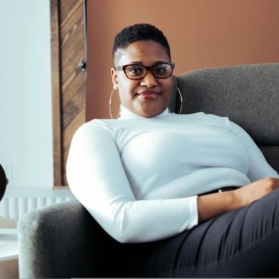 Person sitting in a meditative pose with eyes closed in a bright space.